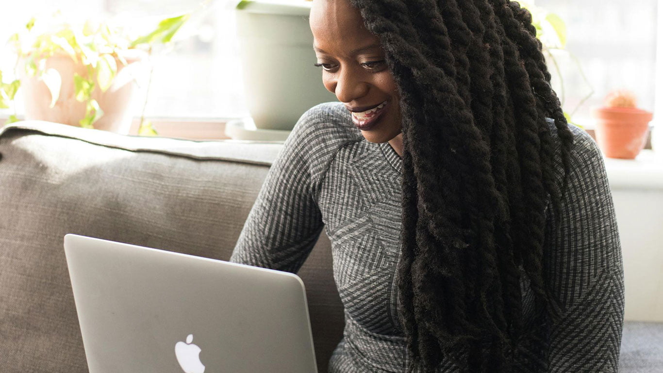 Capa dos cursos online, mulher olhando computador sentada no sofa de sua sala sorrindo